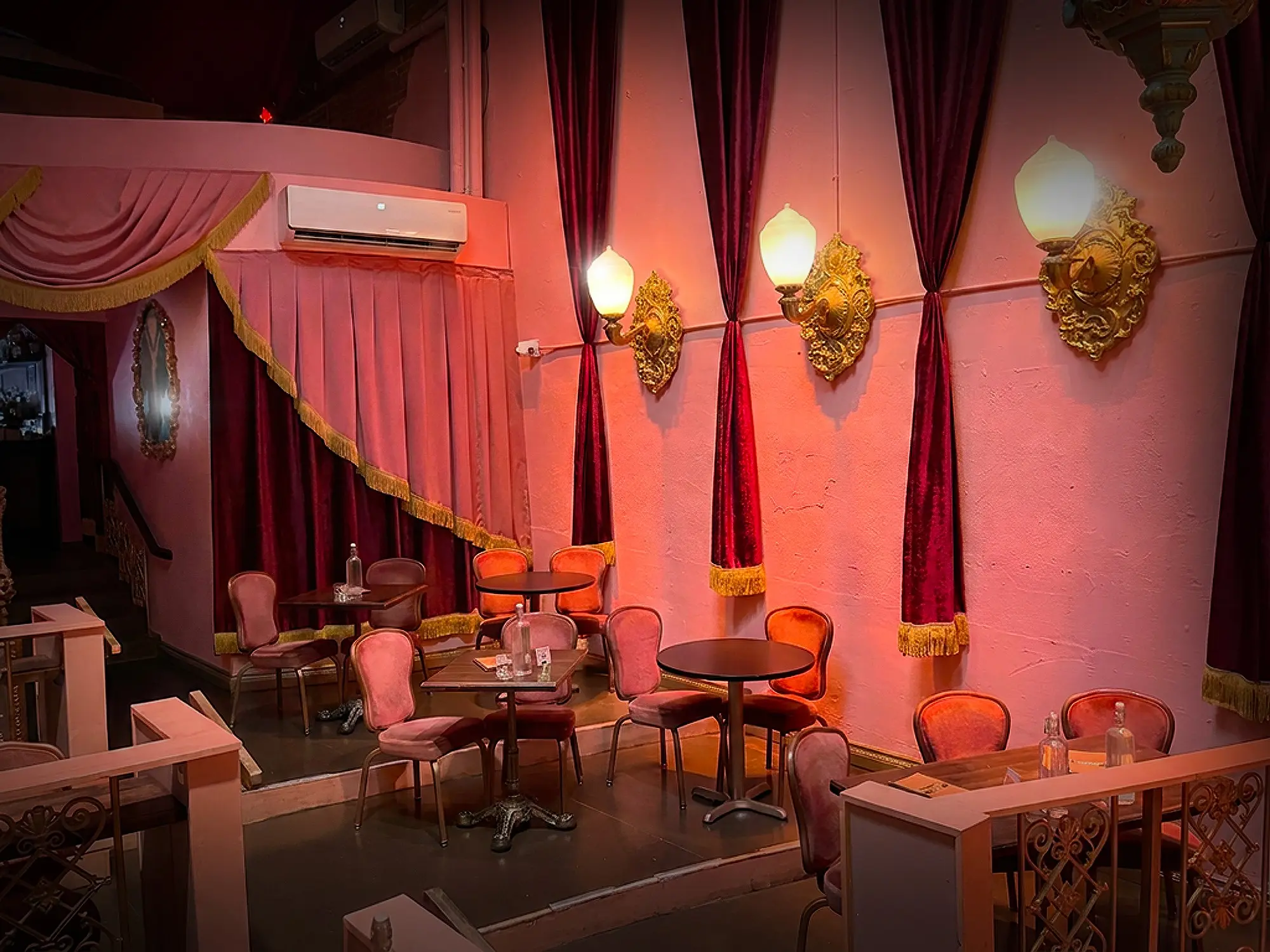 The Paris Theatre interior with deep red drapery, warm pink walls, and restored decorative lighting.